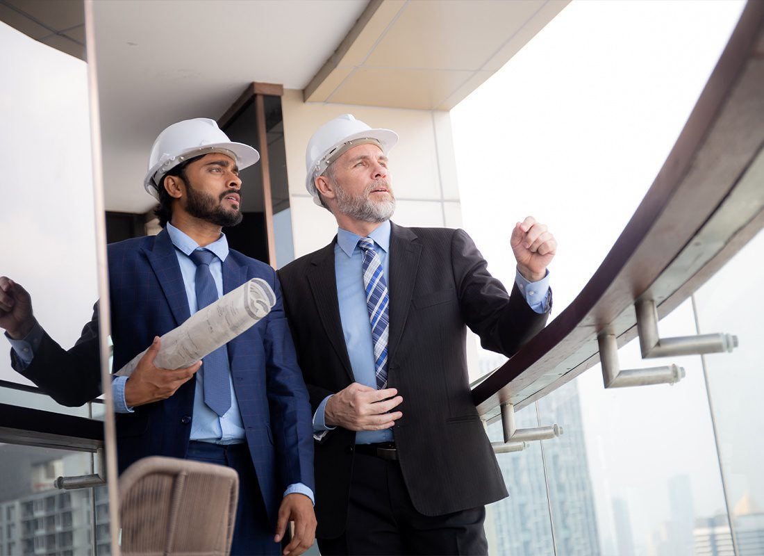 Insurance Solutions - Senior Architect Inspector Talking With Contractor at the Office While Holding Blueprint