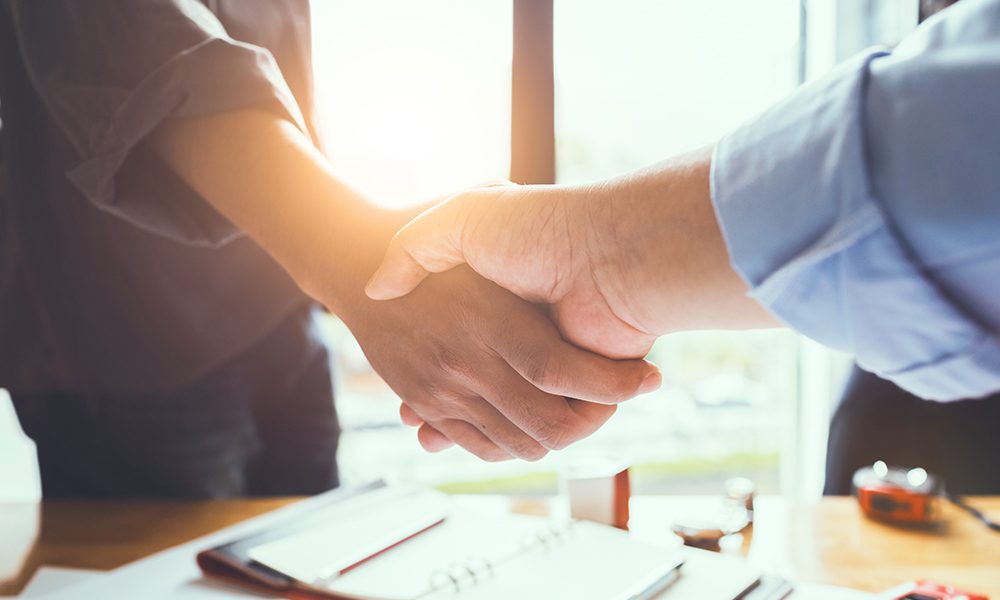 Blog - Close Up of Two People Shaking Hands in an Office Over a Desk