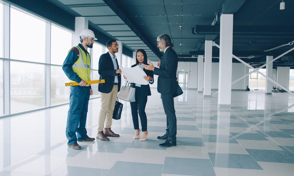 The Importance of Verifying Contractors' Insurance for Property Managers and Building Owners in New York - Building Owner and Property Managers Standing In A Building With A Contractor Looking At Plans