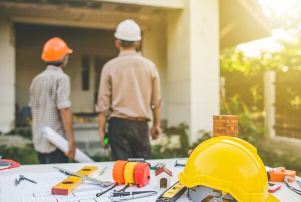 Steer Clear/ Why You Should Avoid Contractors with Questionable Insurance Carriers in New York - Contractors looking at a house with plans and tools in the foreground on a table