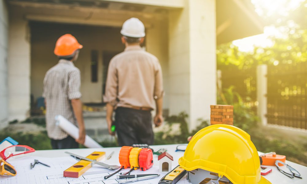 Steer Clear/ Why You Should Avoid Contractors with Questionable Insurance Carriers in New York - Contractors looking at a house with plans and tools in the foreground on a table