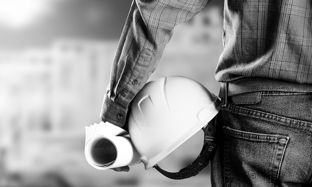 The Importance of Action Over Coverage in New York Construction worker holding his hard hat at his hip with plans in his hand