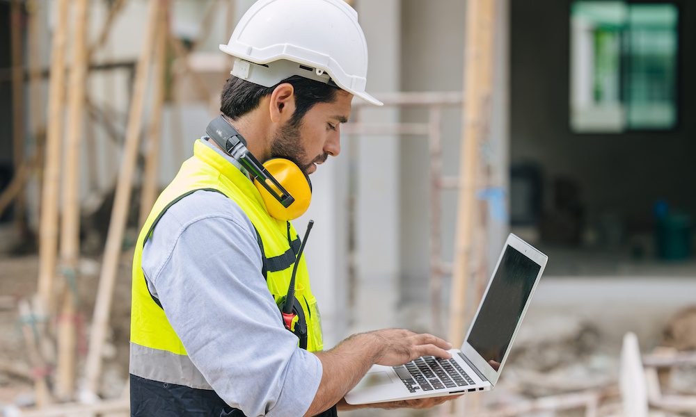 The Importance of Cyber Insurance for General Contractors - Contractor on a job site standing with a laptop working